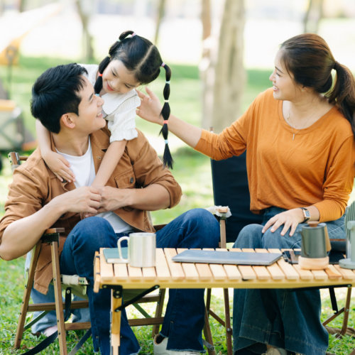 Joyful Asian family camping in a sunny garden, bonding over BBQ,